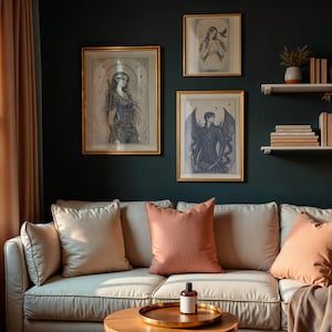 May include: A living room scene featuring a cream-colored sofa with peach-colored pillows and a round wooden coffee table. Above the sofa, three framed art prints with gold frames hang on a dark teal wall. The room is decorated with plants and books.