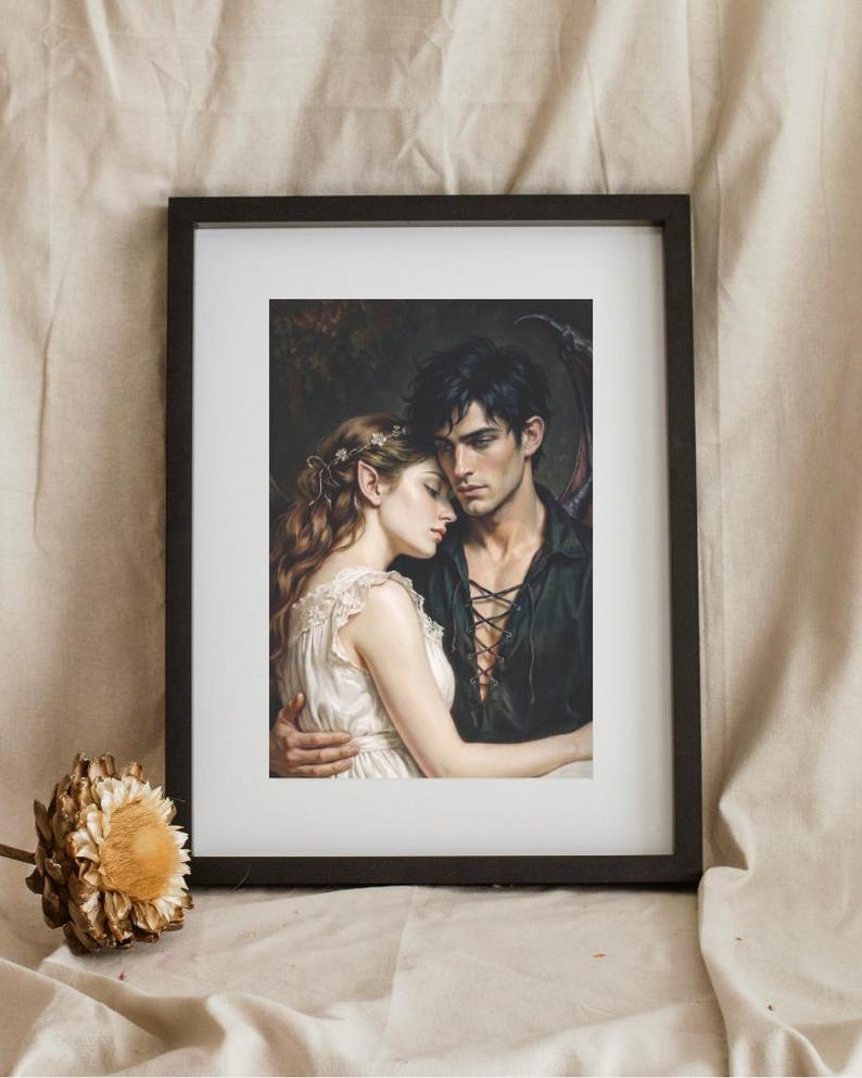 May include: A framed art print featuring a fantasy illustration of a woman with pointed ears and a white dress embracing a man with dark hair and a black lace-up shirt. The man has dark wings visible behind him. The print is in a black frame.