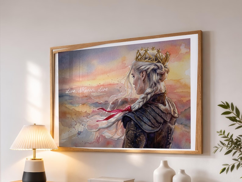 May include: Watercolor print of a woman with long, white braided hair, wearing a gold crown and armor, set against a sunset backdrop. The artwork is framed in a light brown wooden frame. The text "Live, Warm, Live" is visible.