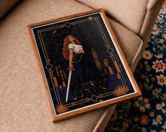May include: Framed art print featuring a woman with red hair holding a sword, set against a night sky with city silhouettes. The artwork is framed in a wooden frame with a white border. The art has a gold geometric border.