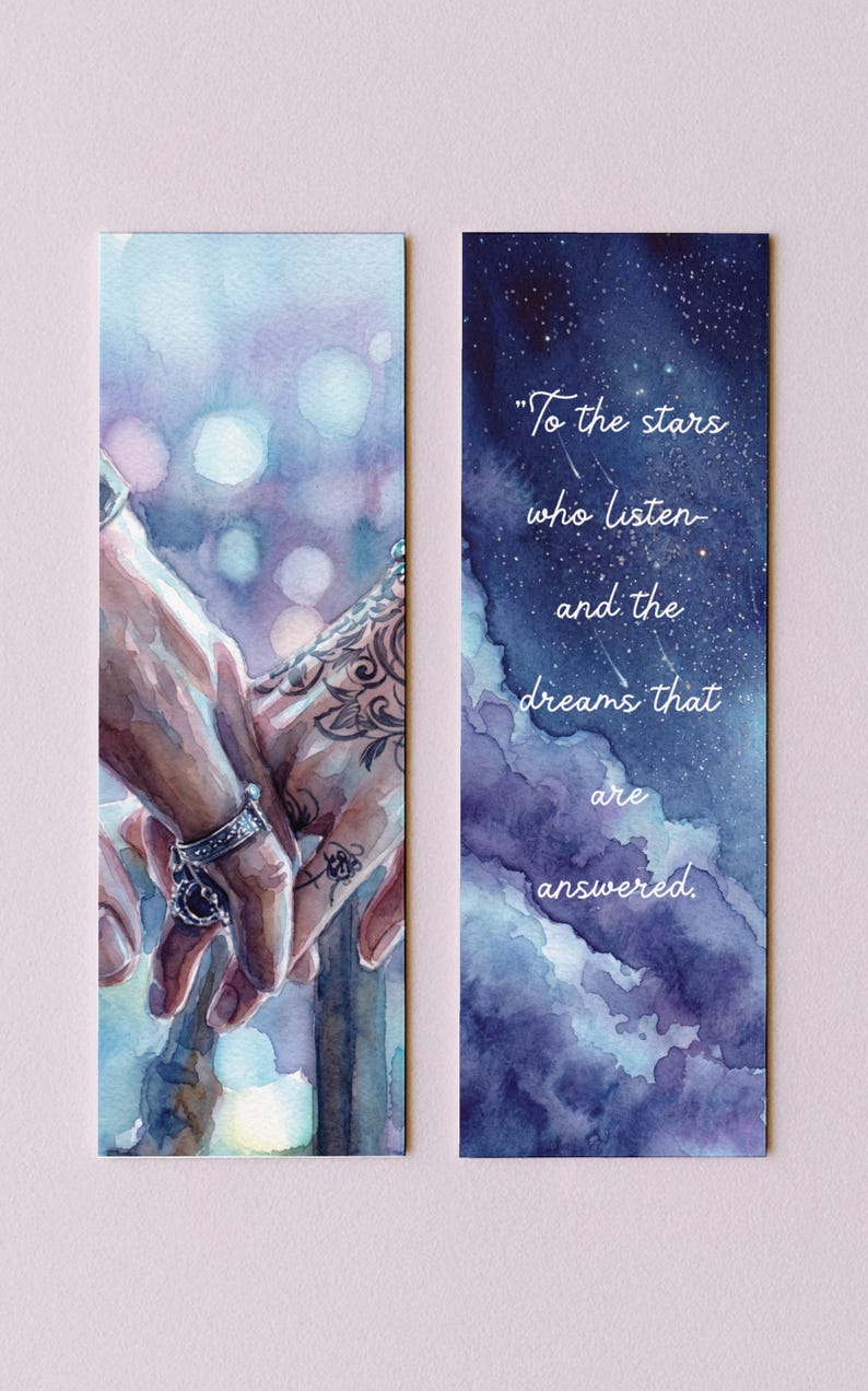 May include: Two watercolor bookmarks. One features hands holding each other, with intricate tattoos and rings. The other has a starry night sky with the quote, "To the stars who listen and the dreams that are answered."