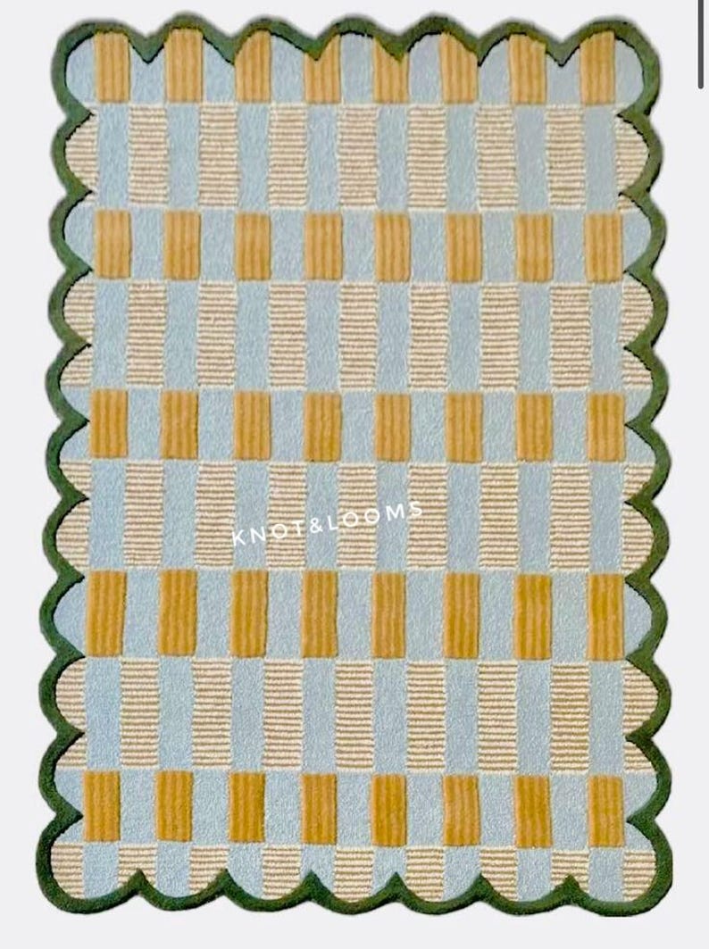 May include: A rectangular rug with a checkered pattern in light blue, tan, and mustard yellow. The rug has a scalloped green border and the text "KNOT & LOOMS" is visible. The rug's design features vertical and horizontal rectangles.