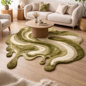 Könnte beinhalten: Ein abstrakter Teppich in Grün- und Cremetönen mit einem fließenden, organischen Design. Die Form des Teppichs ähnelt einer geschmolzenen oder flüssigen Form. Er liegt auf einem Holzboden in einem Wohnzimmer, mit Sofa und Couchtisch im Hintergrund.