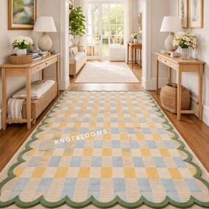 May include: A rectangular rug with a checkered pattern in yellow and pale blue, edged with a green scalloped border. The rug is in a hallway with wooden flooring and furniture. The text "KNOT & LOOMS" is visible on the rug.
