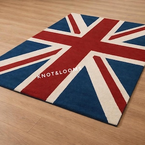 Puede incluir: Una alfombra rectangular con el diseño de la bandera británica. La alfombra tiene un fondo azul, una cruz roja y rayas diagonales blancas. El texto "KNOT & LOOMS" es visible en la alfombra.
