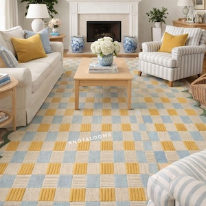 May include: A living room with a patterned rug in yellow, pale blue, and cream, with a green scalloped edge. The room includes a white sofa, a striped armchair, and a wooden coffee table. The rug's pattern is a checkerboard design.