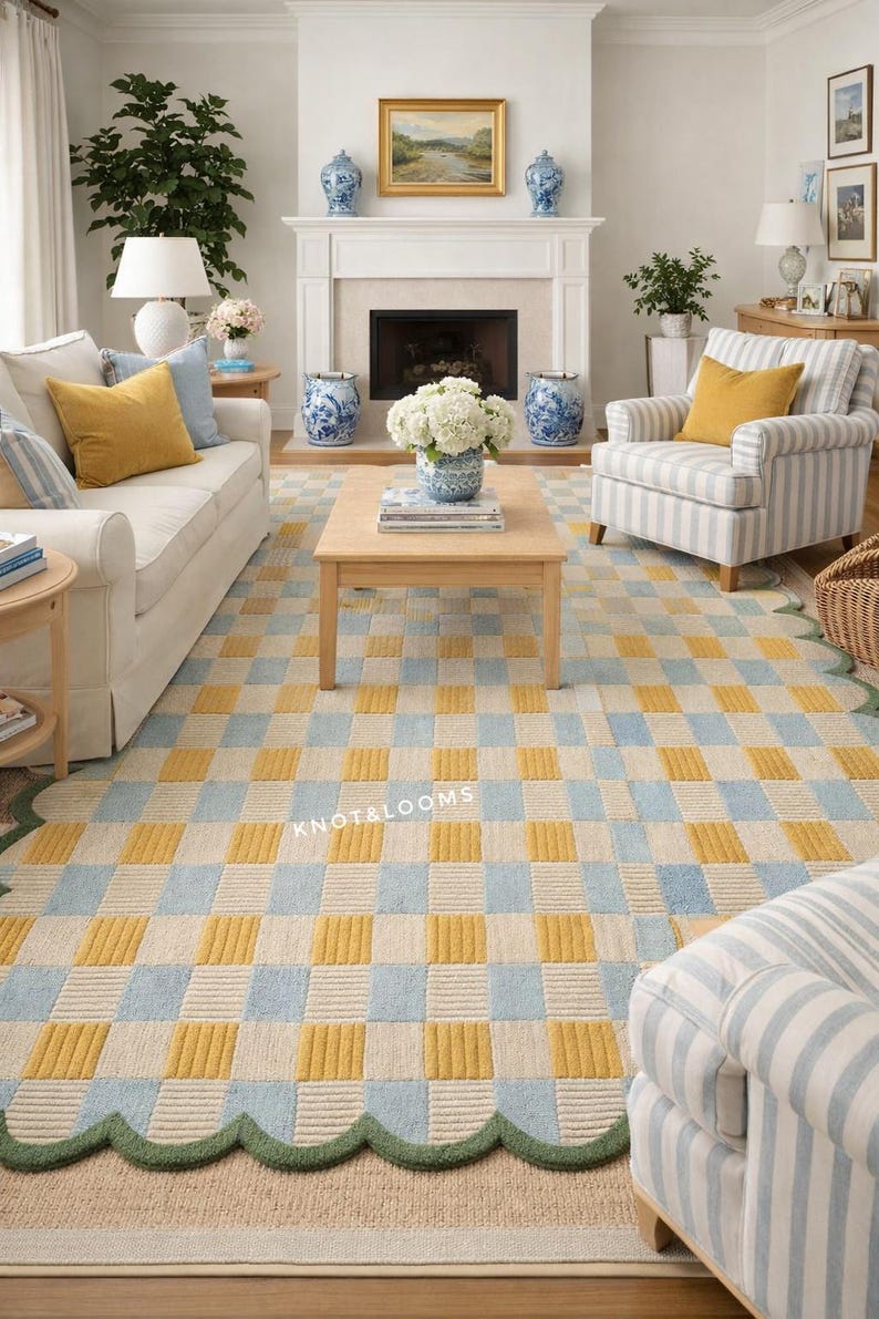 May include: A living room with a patterned rug in yellow, pale blue, and cream, with a green scalloped edge. The room includes a white sofa, a striped armchair, and a wooden coffee table. The rug's pattern is a checkerboard design.