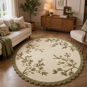 May include: A circular rug in cream with a floral pattern in green and white. The rug has a scalloped border and is on a wooden floor. The rug is in a living room setting.