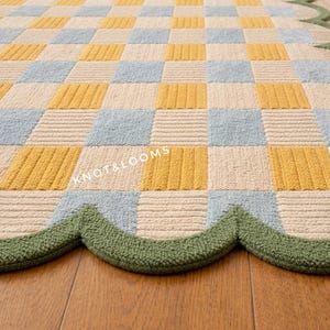 May include: A colourful rug featuring a checkerboard design in yellow, light blue, and cream. The rug has a scalloped green border and the text "KNOT&LOOMS" is visible. Suitable for a living room or bedroom.