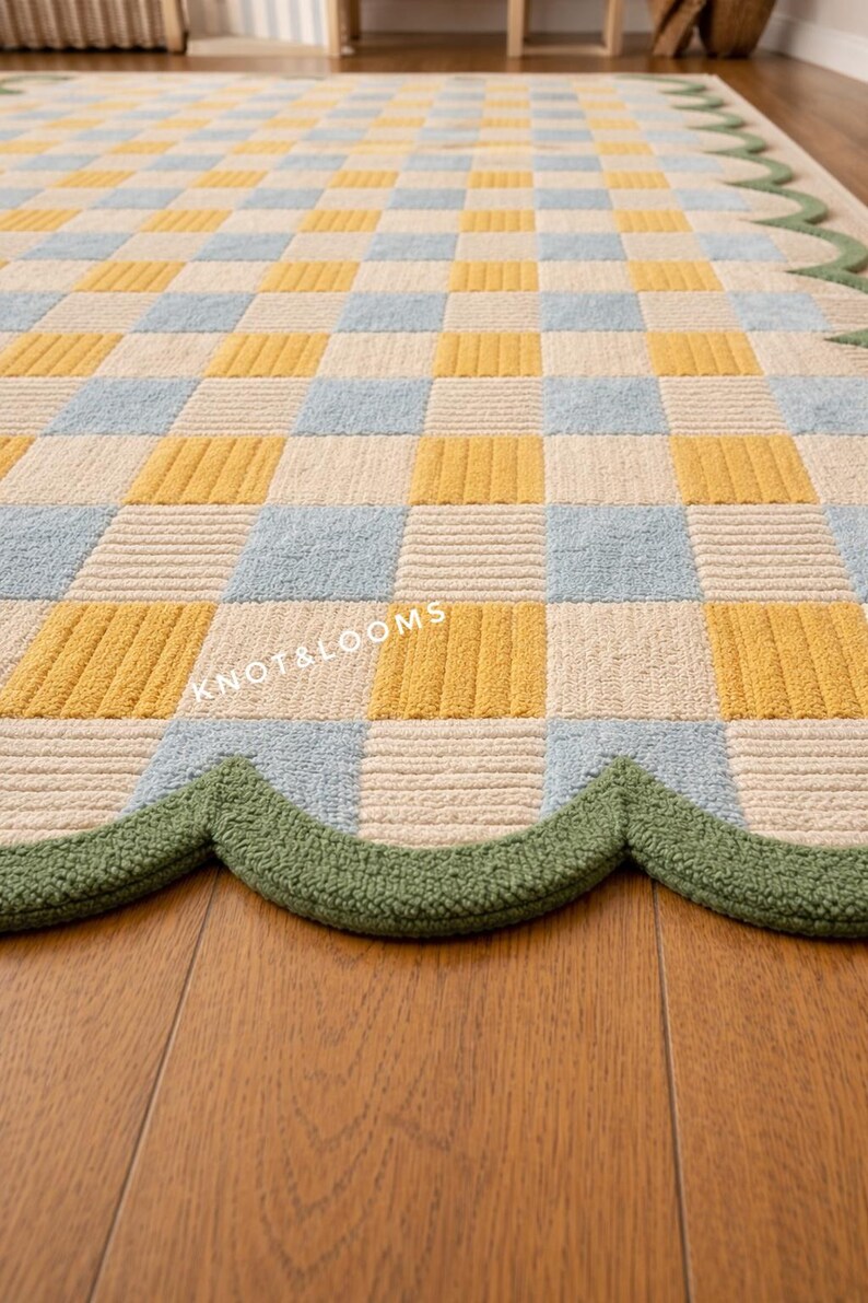 May include: A colourful rug featuring a checkerboard design in yellow, light blue, and cream. The rug has a scalloped green border and the text "KNOT&LOOMS" is visible. Suitable for a living room or bedroom.