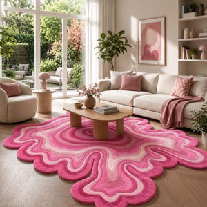 May include: An irregular, organic-shaped area rug featuring concentric, wavy bands of varying shades of pink, ranging from deep magenta to soft blush, creating a fluid, layered effect across the floor surface in a living room setting.