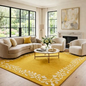 May include: A living room featuring a curved beige sofa, two cream armchairs, and a round coffee table. A vibrant yellow rug with a white floral border is on the floor. Large windows and a fireplace complete the scene.