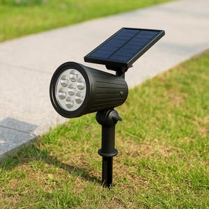 Pode incluir: Um holofote preto movido a energia solar com um pequeno painel solar e um grupo de luzes LED. O holofote é montado em uma estaca preta, projetado para uso ao ar livre em um jardim ou quintal. O fundo mostra grama verde e uma passarela pavimentada.