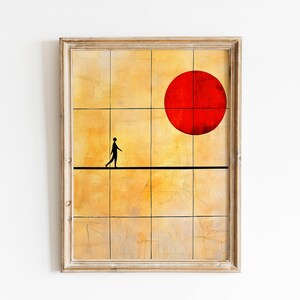 Puede incluir: Impresión artística enmarcada con un diseño minimalista. Una figura silueteada camina sobre una cuerda floja contra un fondo amarillo y naranja, con un gran círculo rojo. La obra está en un marco de madera clara. Medidas en centímetros.