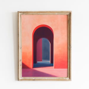 Op de afbeelding: Ingelijste kunstdruk met een reeks bogen in tinten rood, roze en blauw. Het kunstwerk heeft een minimalistische stijl, met sterke schaduwen en een focus op geometrische vormen. De lijst is licht goudkleurig.