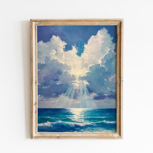 May include: A framed painting depicts a seascape with a bright sky and ocean. The sky is filled with fluffy white and blue clouds, with sunlight breaking through. The ocean is a deep blue with white-capped waves.