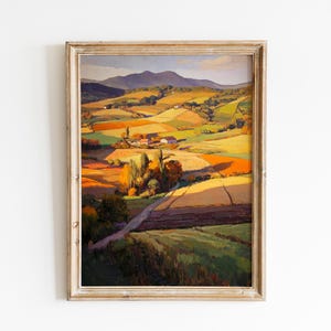 May include: A framed landscape painting depicting rolling hills and valleys in shades of green, yellow, and orange. A road winds through the fields towards a small village. The artwork is in a rustic, light-colored wooden frame.