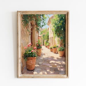 May include: An oil painting in a wooden frame shows a sunlit alley with stone walls and terracotta pots of pink flowers. Green vines hang overhead, casting shadows on the cobbled path.