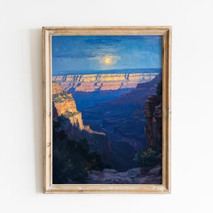 Op de afbeelding: Ingelijst landschapsschilderij van de Grand Canyon in de schemering. Het kunstwerk heeft een levendig kleurenpalet met tinten blauw, oranje en paars. De gelaagde rotsformaties van de canyon worden verlicht door de ondergaande zon, met een heldere maan aan de hemel.