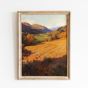 May include: A framed landscape painting depicts a valley scene with rolling hills and a field of golden wheat. The artwork features warm tones of yellow, orange, and brown, with hints of green and blue. The painting is in a distressed, light-colored wooden frame.
