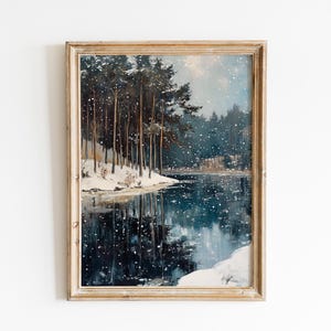 May include: Framed vintage winter landscape painting. The artwork depicts a snowy scene with tall, dark trees lining the edge of a lake. The water reflects the trees and falling snow. The frame is a light brown color.