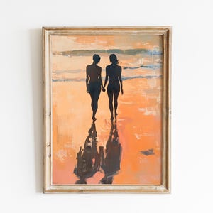 Puede incluir: Pintura enmarcada de dos figuras silueteadas tomadas de la mano, caminando por una playa. La obra de arte presenta tonos cálidos de naranja y amarillo, con reflejos en la arena mojada. El marco es de madera clara envejecida.
