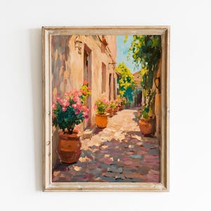 May include: Oil painting depicting a sunlit alleyway with buildings and potted plants. The artwork features a warm colour palette with pink flowers and terracotta pots. The painting is framed in a light-coloured wooden frame.