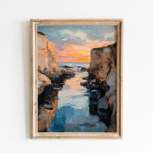 May include: Oil painting of a coastal scene with a sunset. The artwork depicts a narrow waterway between two cliffs, with the sky ablaze with orange and yellow hues. The painting is framed in a vintage-style, light-colored wooden frame.