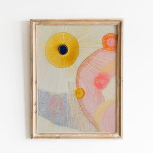 May include: Abstract art print in a wooden frame. The artwork features a yellow sun with a dark blue center, a pink and orange shape, and other colorful details. The frame has a distressed, vintage look.