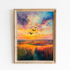 May include: Framed landscape painting depicting a vibrant sunset with a flock of birds in flight. The artwork features a field of golden grass and colorful clouds in shades of orange, pink, and purple. The frame is a light, distressed wood.