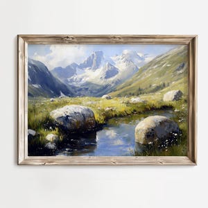 May include: A framed landscape painting depicts a mountain scene with a river. The artwork features a light brown wooden frame. The painting showcases snow-capped mountains, green hills, a blue river, and large rocks in a field of grass.