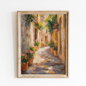 May include: Framed oil painting of a sunlit alleyway. The artwork depicts a narrow street with stone walls, lined with potted plants and flowers. The painting is in a distressed, light-coloured wooden frame.
