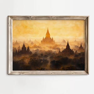 以下が含まれることがあります： 古代寺院の風景に金色の日の出を描いた額入りのプリント。霧のかかった木々が生い茂る谷から現れる複数のパゴダ様式の構造物と、暖かく黄色い空が特徴です。フレームは明るい色の木材で作られています。