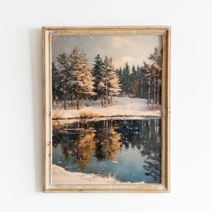May include: A framed vintage winter landscape painting. The artwork depicts a snowy scene with a reflective lake, snow-covered trees, and a forest in the background. The painting has a warm color palette with a light-colored wooden frame.