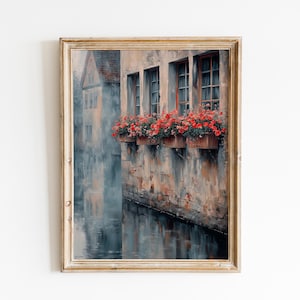 Puede incluir: Pintura a la acuarela enmarcada de una escena de canal europeo. La obra representa un edificio con ventanas adornadas con flores rojas en jardineras. El edificio se refleja en el agua, creando una atmósfera serena.