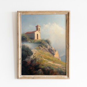 Puede incluir: Pintura de paisaje vintage enmarcada de una iglesia en una colina. La obra presenta una iglesia beige con tejado rojo y campanario, sobre un fondo de cielo nublado y exuberante vegetación. La pintura está en un marco de madera envejecida.