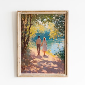 Puede incluir: Pintura enmarcada que representa a una pareja caminando de la mano por un sendero junto a un lago. La obra de arte presenta una paleta de colores cálidos con la luz del sol filtrándose a través de los árboles, creando una escena romántica. El marco es de madera clara envejecida.