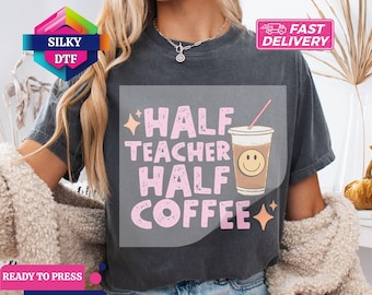 May include: Dark gray t-shirt with the text "Half Teacher Half Coffee" in pink, along with a coffee cup graphic. The shirt has a relaxed fit and short sleeves. The design includes star accents.