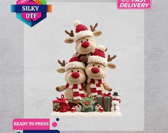 Op de afbeelding: Een stapel van drie rendierknuffels met rood-witte gestreepte sjaals en kerstmutsen. De afbeelding bevat ingepakte cadeaus, ornamenten en een sneeuwpop. De tekst "SILKY DTF" en "READY TO PRESS" is inbegrepen.