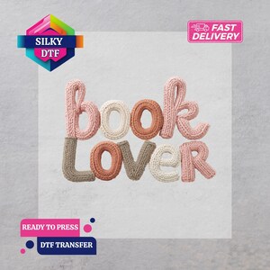 May include: A DTF transfer featuring the words "book lover" in a knitted style. The word "book" is in pink, white, and brown, while "lover" is in brown, white, and pink. The image includes the text "Silky DTF", "Fast Delivery", "Ready to Press", and "DTF Transfer".