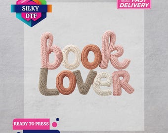 May include: A DTF transfer featuring the words "book lover" in a knitted style. The word "book" is in pink, white, and brown, while "lover" is in brown, white, and pink. The image includes the text "Silky DTF", "Fast Delivery", "Ready to Press", and "DTF Transfer".