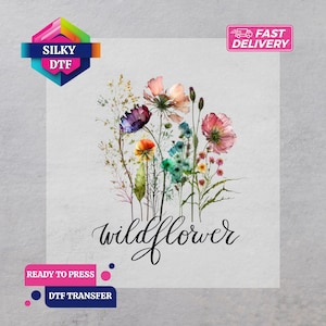 Op de afbeelding: DTF-transfer met een aquarel illustratie van wilde bloemen in roze, paars, oranje en blauw. Het woord "wildflower" is geschreven in elegant script. De afbeelding bevat ook de tekst "Silky DTF" en "Ready to Press".