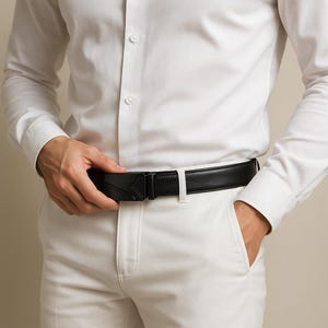 Puede incluir: Cintur&oacute;n de cuero negro con hebilla geom&eacute;trica. El cintur&oacute;n se lleva con pantalones blancos y una camisa blanca abotonada. La hebilla tiene un dise&ntilde;o angular &uacute;nico.