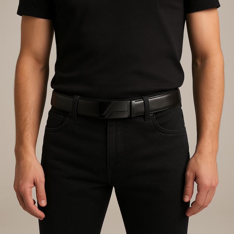 Puede incluir: Cintur&oacute;n de cuero negro con hebilla geom&eacute;trica. El cintur&oacute;n se lleva con vaqueros negros y una camiseta negra. La hebilla tiene una forma angular &uacute;nica.