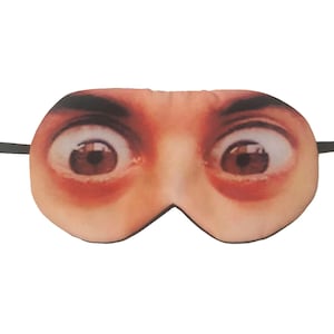 May include: A novelty sleep mask printed with a realistic image of wide, startled eyes. The mask is beige with brown eyes and black elastic straps. This humorous accessory is designed to block out light for sleep.