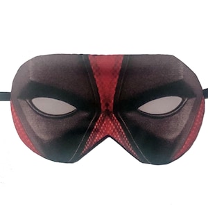 May include: A sleep mask featuring a design inspired by a comic book character. The mask is primarily black with red accents, including a central stripe and a textured pattern. It has white eye openings and a black elastic strap.