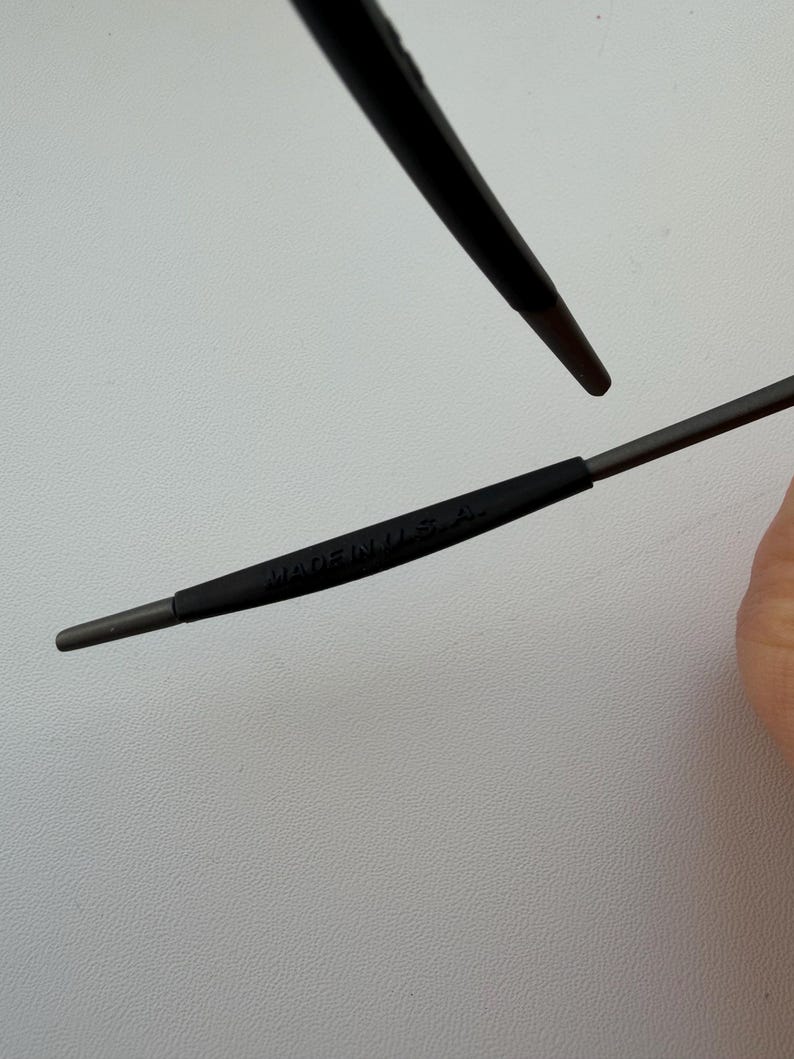 May include: Close-up of a pair of dark gray eyeglasses. The text "MADE IN U.S.A." is printed on the temple arm. The frame is a dark gray color.
