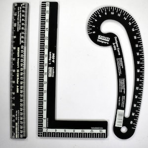 Puede incluir: Tres herramientas de medición negras: una regla de 30 cm, una escuadra en L y una regla curva. Las herramientas tienen marcas y texto en blanco, incluida la marca "KHYATI Designer's". La regla curva mide hasta 40 cm.