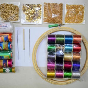 May include: A craft kit with various sewing and embroidery supplies. Includes spools of colourful thread, needles, a wooden embroidery hoop, beads, sequins, and a white spool of thread labelled "dolphin".