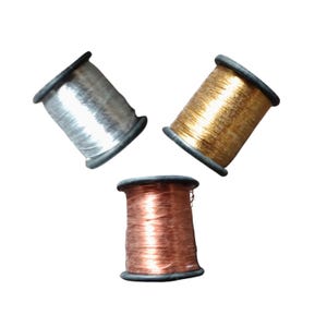 Peut inclure: Trois bobines de fil métallique argenté, doré et cuivré. Chaque bobine a un bord noir et est remplie de fil étroitement enroulé. Les bobines sont disposées en triangle sur fond blanc.